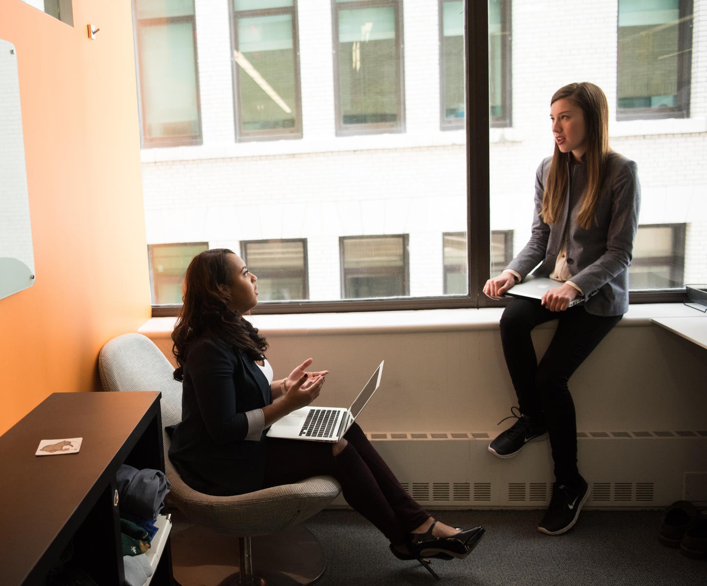 Two women sat discussing in front of a large window