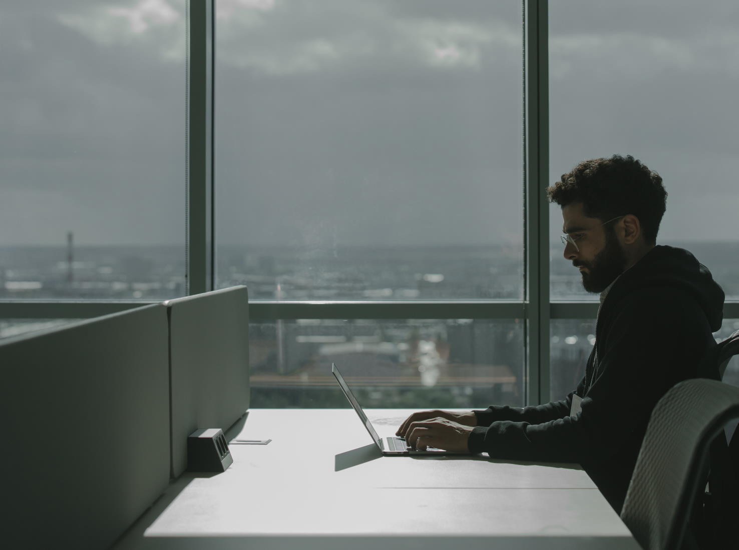 A man working at a laptop in front of a large window