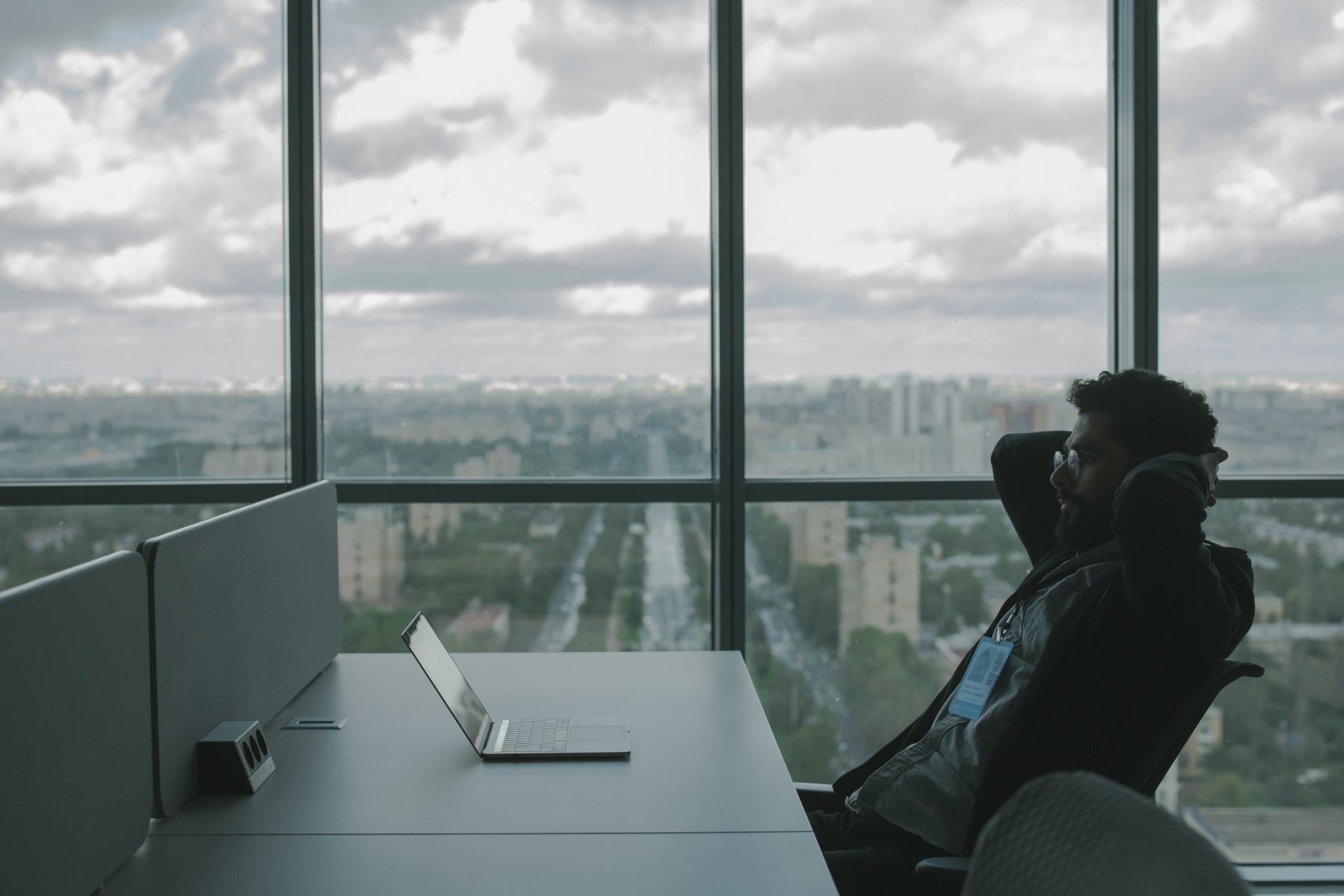 Laptop computer user sitting relaxed with hands behind his head in front of a large window