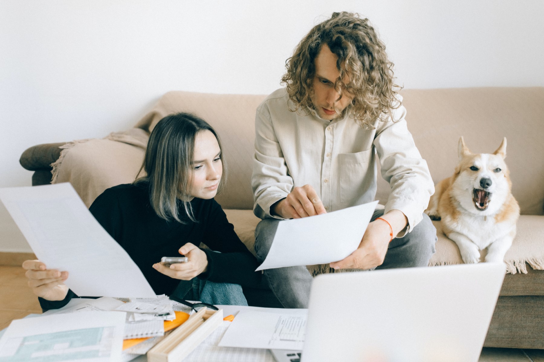 A man and woman sat at their laptops reviewing something on a sheet of paper